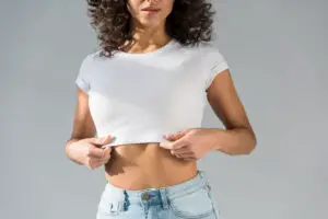 woman wearing white crop top with blue jeans on grey background